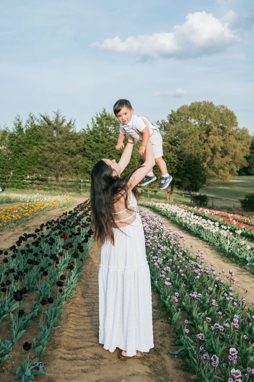 Joyful mother in white dress lifting baby boy high in the air in a tulip field Greensboro NC