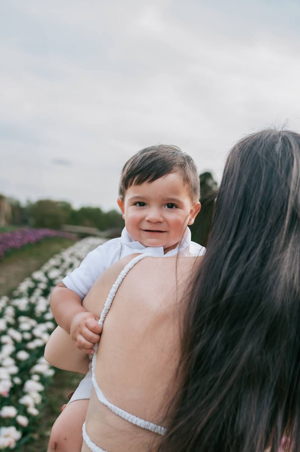 Adorable baby boy smiling over mothers shoulder in a blooming flower field Asheboro NC