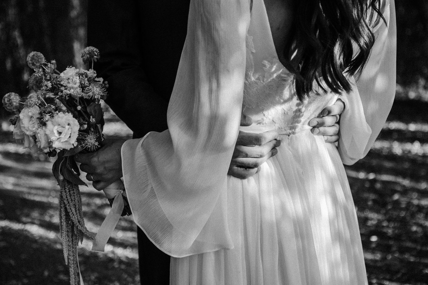 Black and white photo of bride and groom embracing, bride holding a floral bouquet, wearing an elegant white dress.