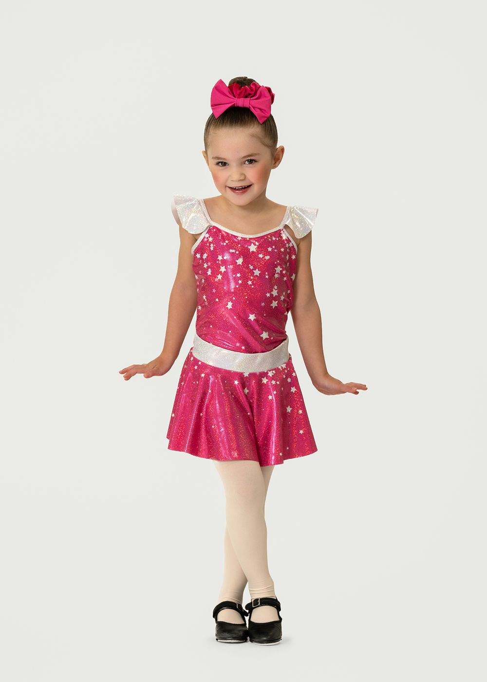 Young girl in pink star-print dance costume with bow headband, white tights, and black tap shoes. Dance photo in Regina, Saskatchewan.