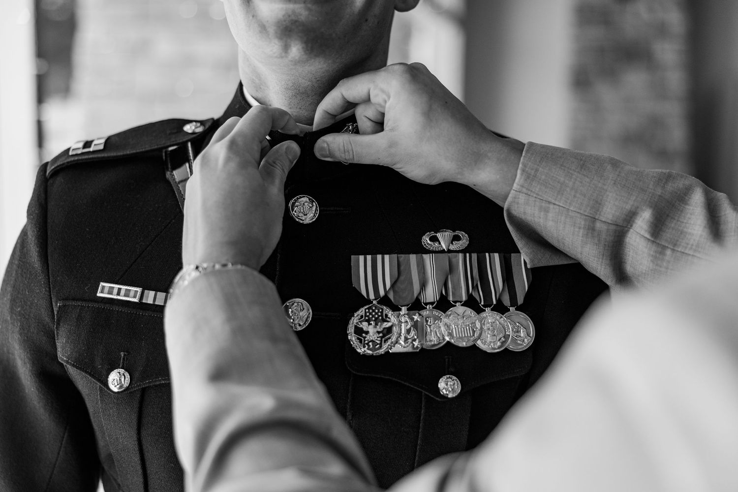 Black and white photo of military officer in dress uniform with medals being adjusted by another person.