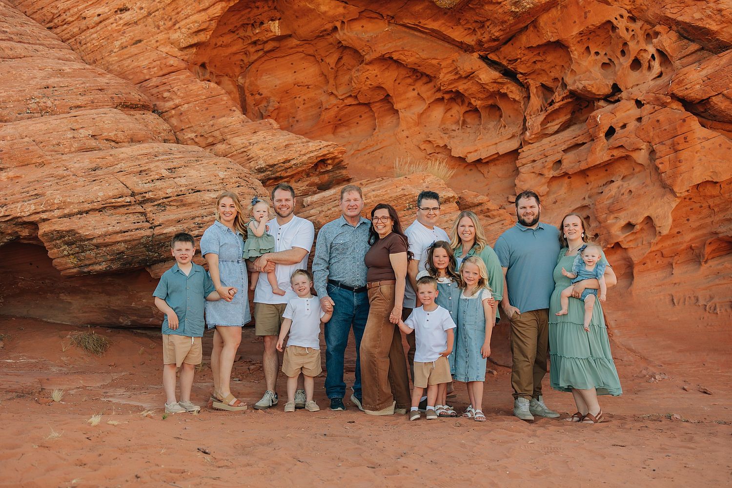 Family group portrait posed in front of red sandstone rock formation in a desert landscape.
