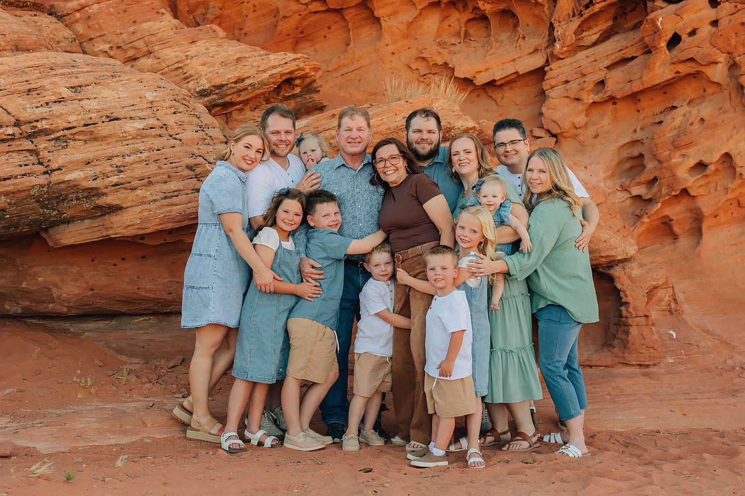 Large family group posing together in front of red rock canyon walls, wearing coordinated blue and green outfits.