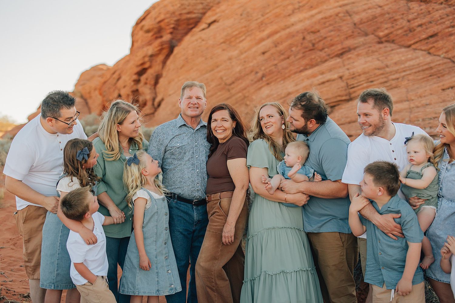 Large family posing together in front of red rock formations in a desert landscape during golden hour.