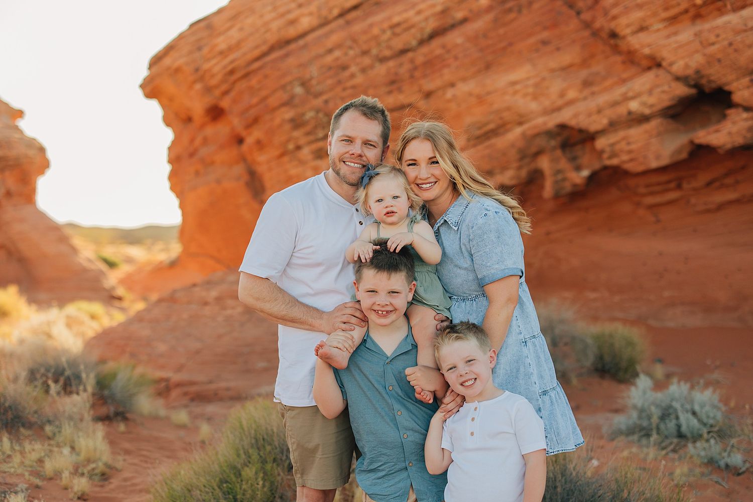 Happy family of five posing together in front of red rock formations during outdoor desert photo session.