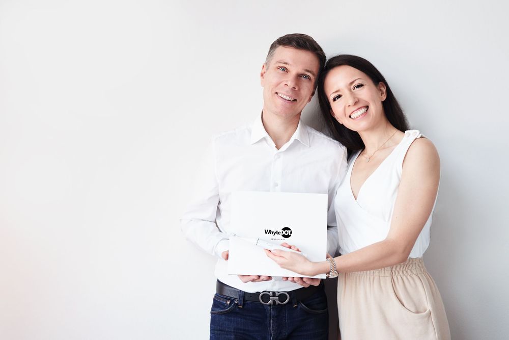 Smiling couple holding a white laptop together against a light grey background.