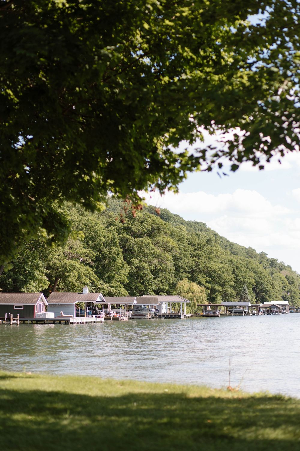 Scenic lakeside view with boat docks and tree-covered hills on a sunny day.