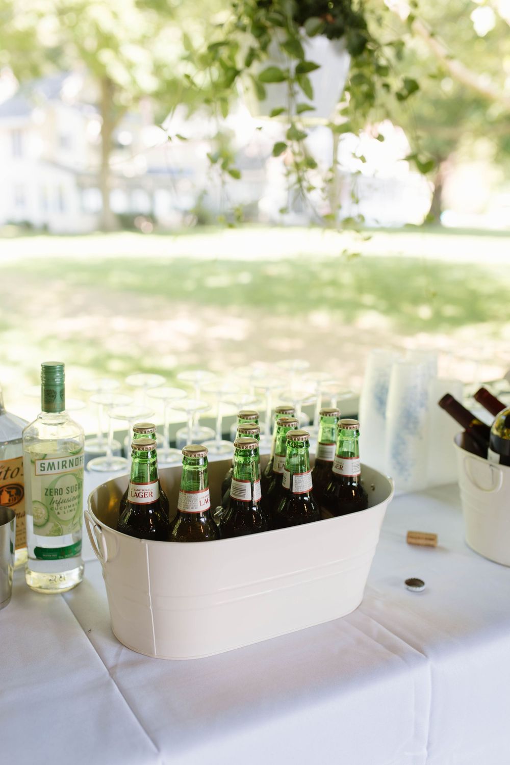 White bucket filled with green beer bottles on outdoor bar table with Smirnoff vodka bottle at garden party.