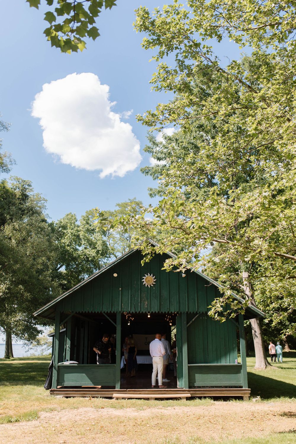A charming green wooden cabin pavilion surrounded by lush trees under a bright blue sky at an outdoor wedding venue.