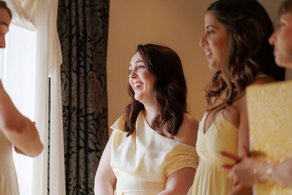Bridesmaids in yellow dresses smile and laugh together during wedding preparations in an elegant room.