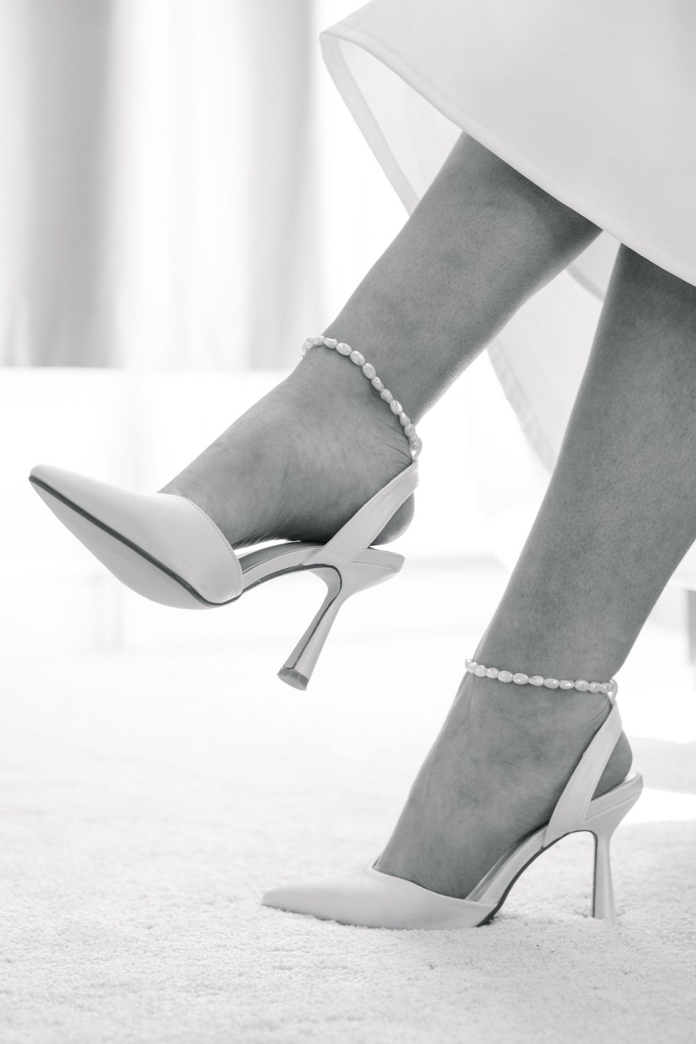 Elegant bridal heels with pearl ankle straps on a woman's feet, captured in black and white photography.