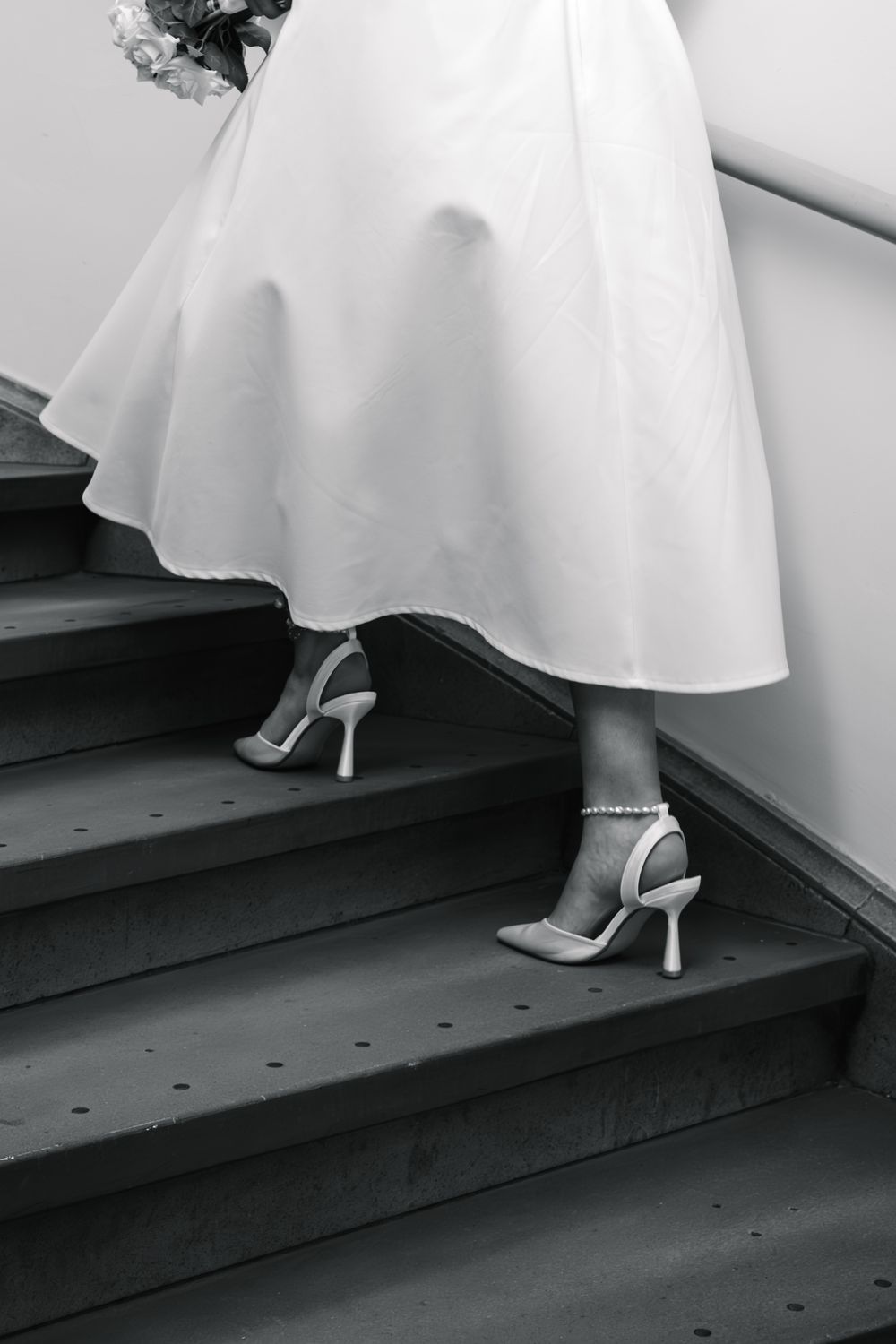 Black and white photo of a bride in a white dress and heels walking up stairs on her wedding day.