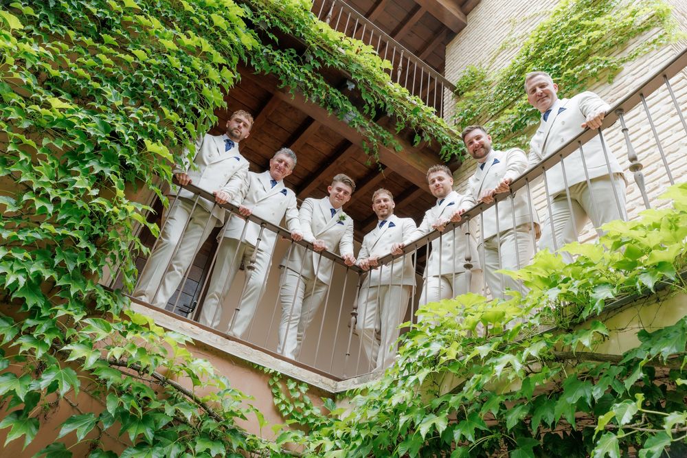 Group of people in white coats posing on ivy-covered balcony, surrounded by lush green vines on a historic building.