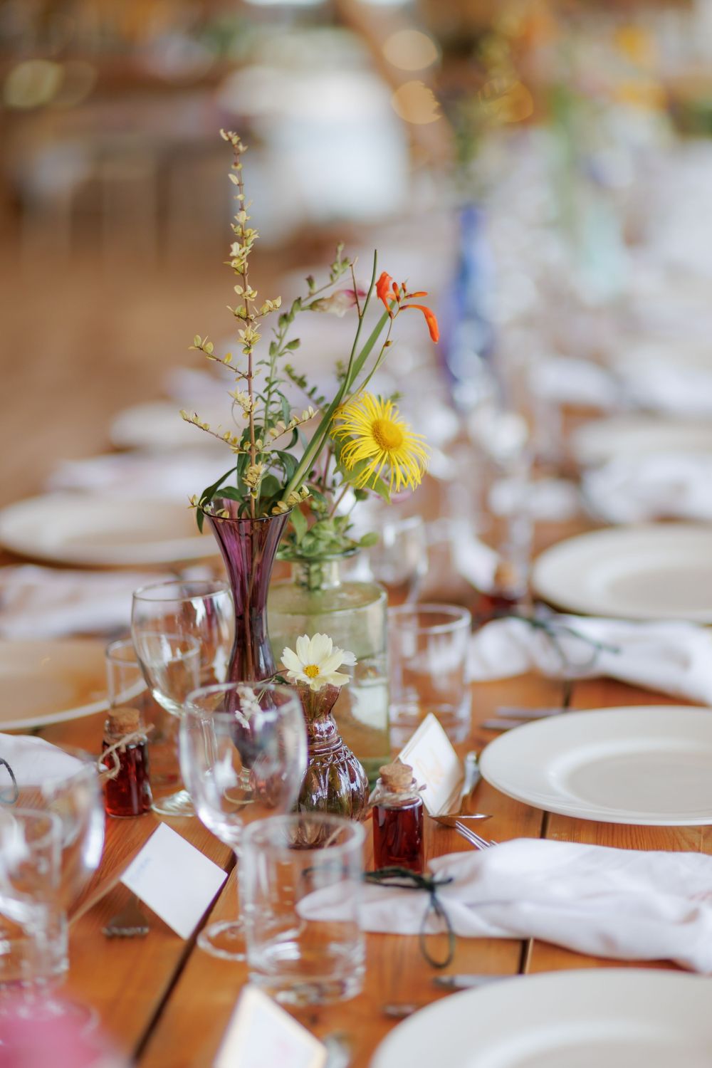 Elegant wedding reception table with wildflower centerpieces, white plates, and glassware on a wooden table.