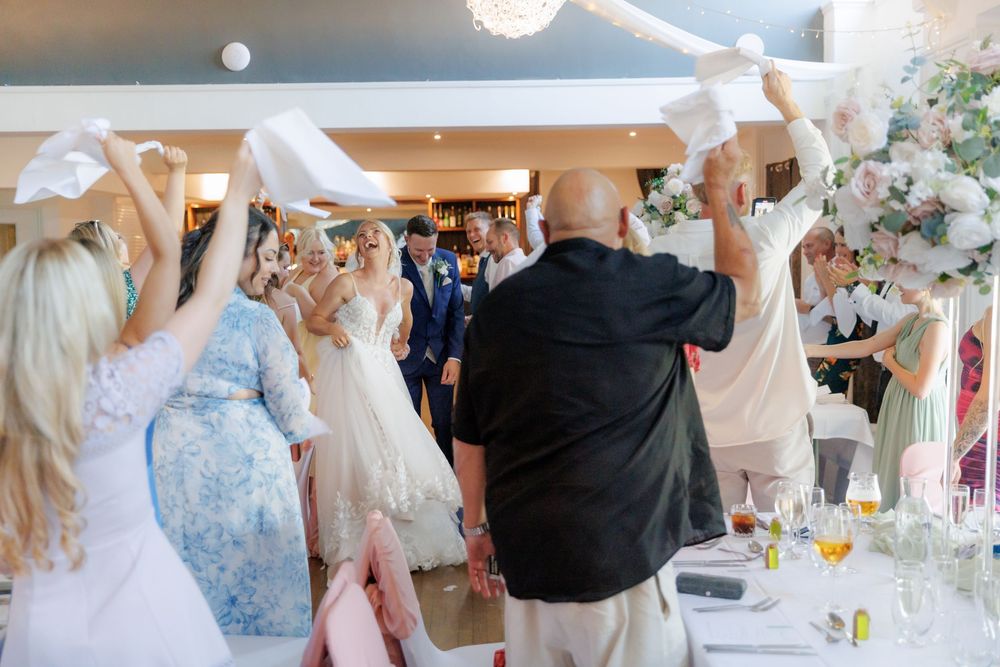 Wedding guests waving white napkins to celebrate bride and groom's entrance into reception venue.
