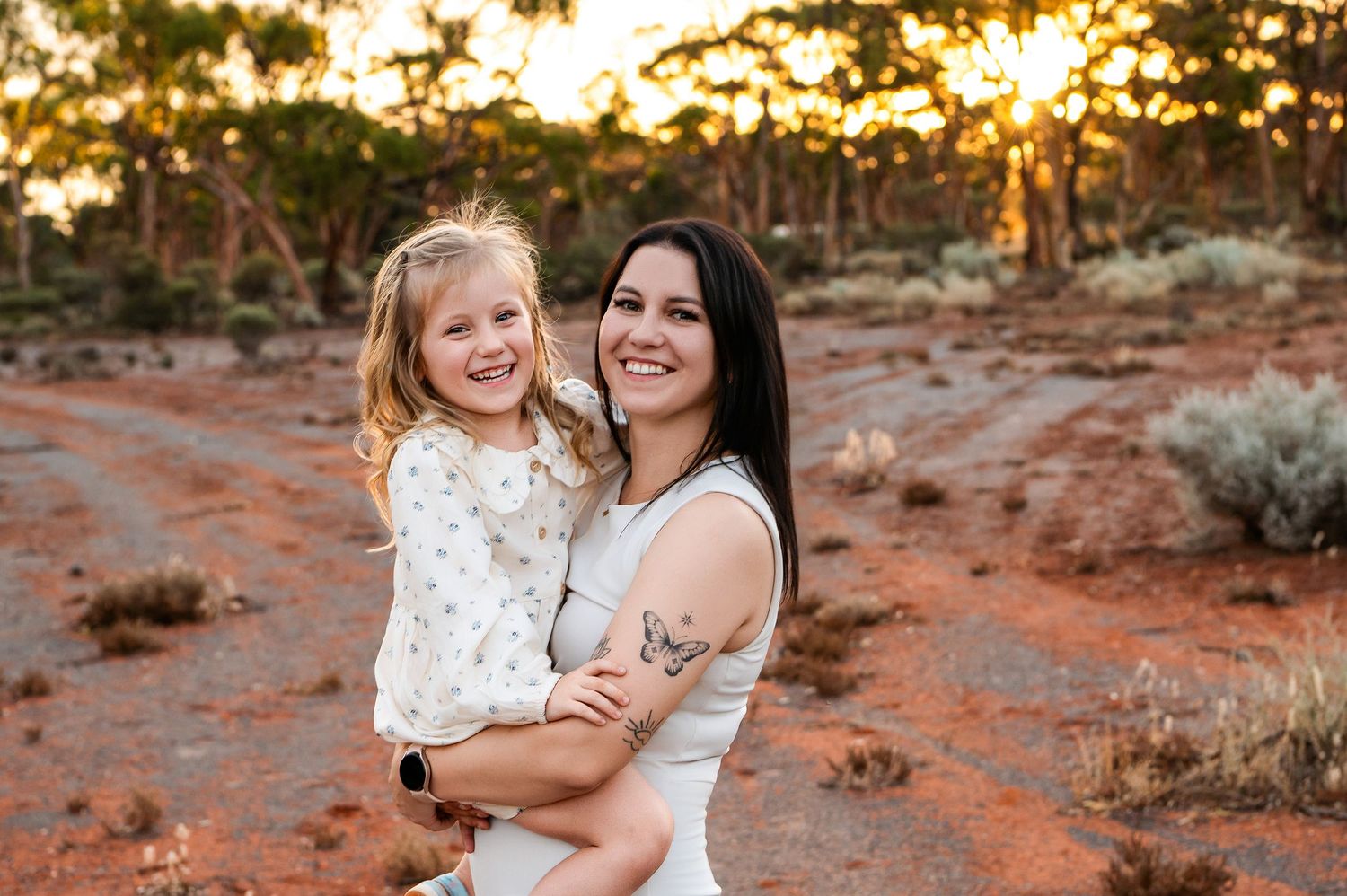 Happy Asian family of three posing outdoors in golden hour light among desert shrubs, parents holding toddler daughter.