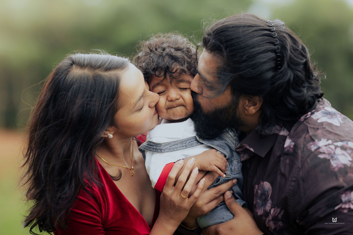 Loving parents kissing their curly-haired toddler on cheeks outdoors in a tender family portrait.