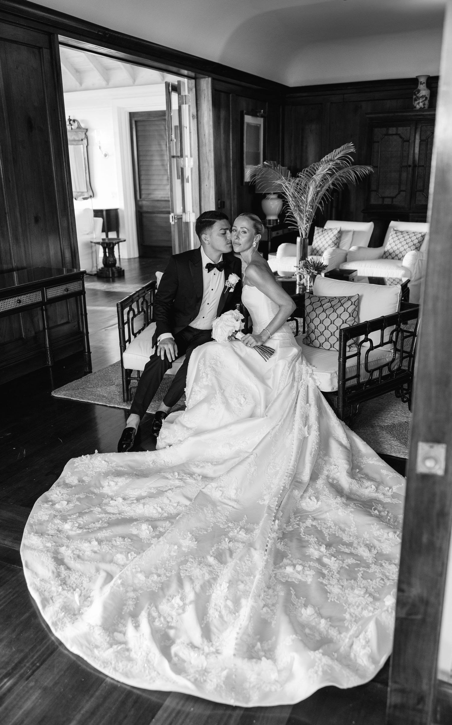 Bride and groom share a kiss while seated in an elegant wood-paneled room with hardwood floors on their wedding day.
