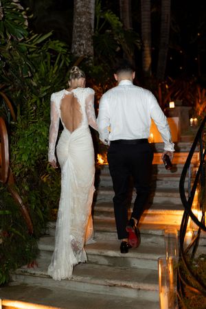 Bride and groom walking up candlelit stairs at night, bride wearing backless lace wedding gown.
