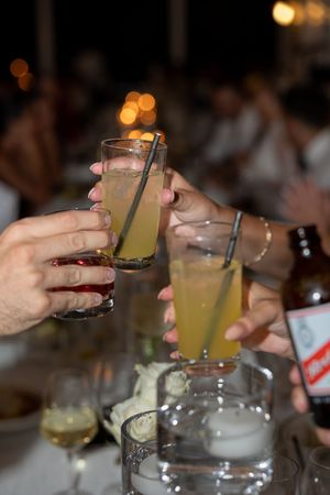 Wedding guests clinking cocktail glasses in a celebratory toast at an elegant outdoor evening reception dinner.