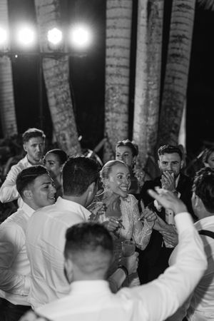 Black and white photo of wedding guests dancing and celebrating joyfully at a lively indoor reception party.