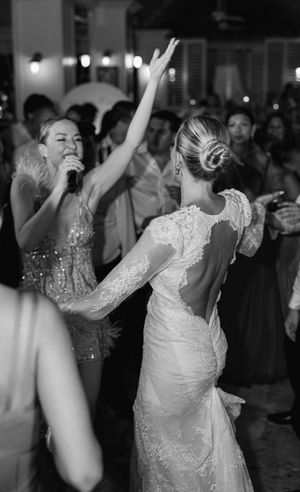 Bride in lace backless gown dancing at wedding reception while singer performs with microphone in black and white photo.