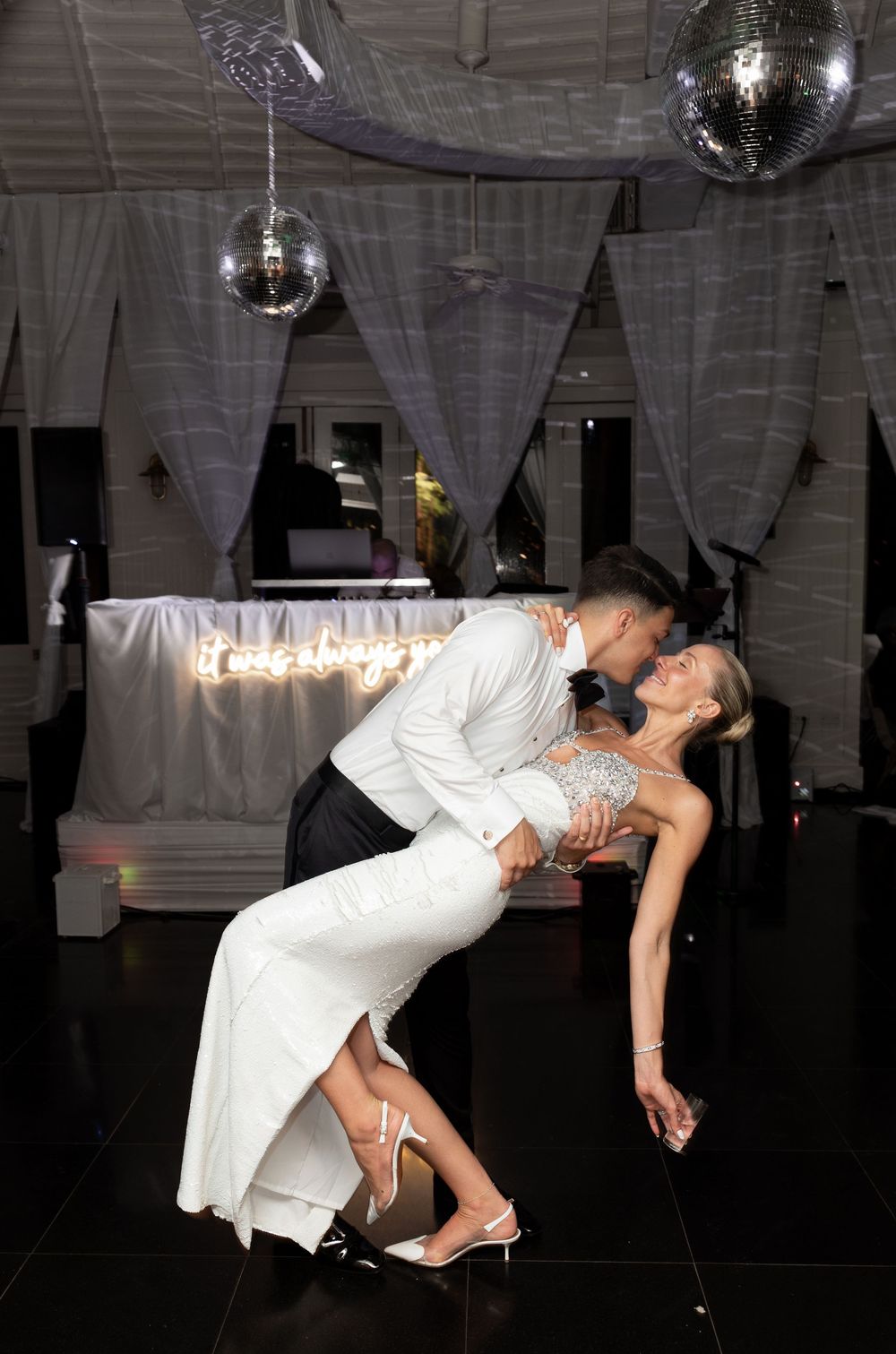 Bride and groom share a romantic dip kiss on the dance floor under sparkling disco balls at their wedding reception.