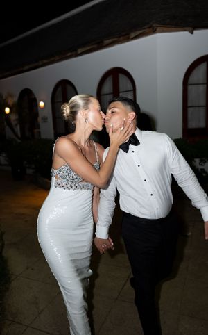 Bride and groom sharing a kiss on the dance floor, she wears a sequined white gown, he wears a tuxedo.
