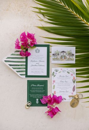 Tropical wedding invitation suite with green and white stationery, pink bougainvillea flowers, and palm leaves on a neutral background.