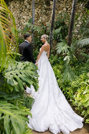 Bride and groom share an intimate moment in a lush tropical garden, bride wearing a stunning white ballgown with long train.