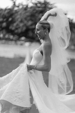 A joyful bride in a strapless white gown and veil laughs outdoors in a black and white wedding photo.