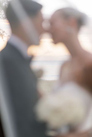 Blurred artistic wedding photo of bride and groom sharing a kiss, bride holding white bouquet.