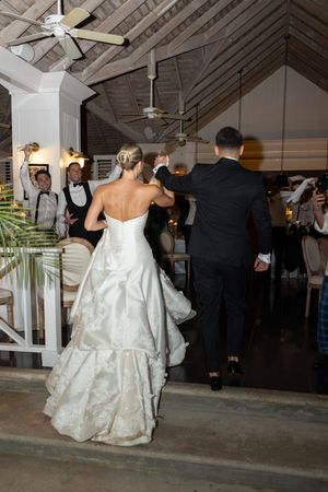 Bride in white strapless gown and groom in black suit make grand entrance at elegant indoor wedding reception.