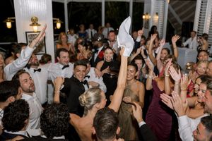 Joyful wedding reception crowd dancing and celebrating with hands raised in elegant venue.