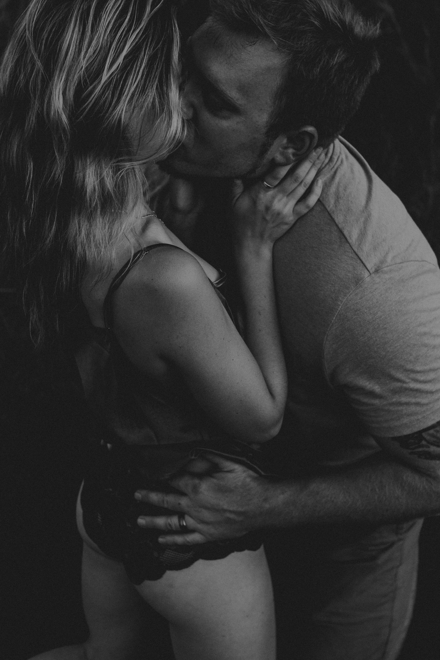 Black and white photo of a couple sharing a passionate kiss while embracing in a romantic, intimate moment.