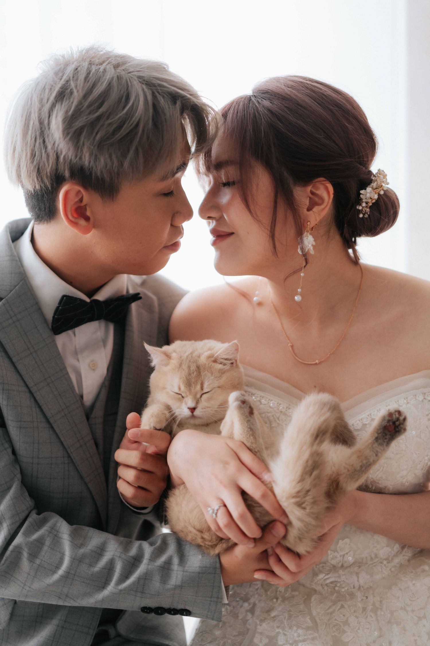 Wedding couple in formal attire holding sleeping cat between them.