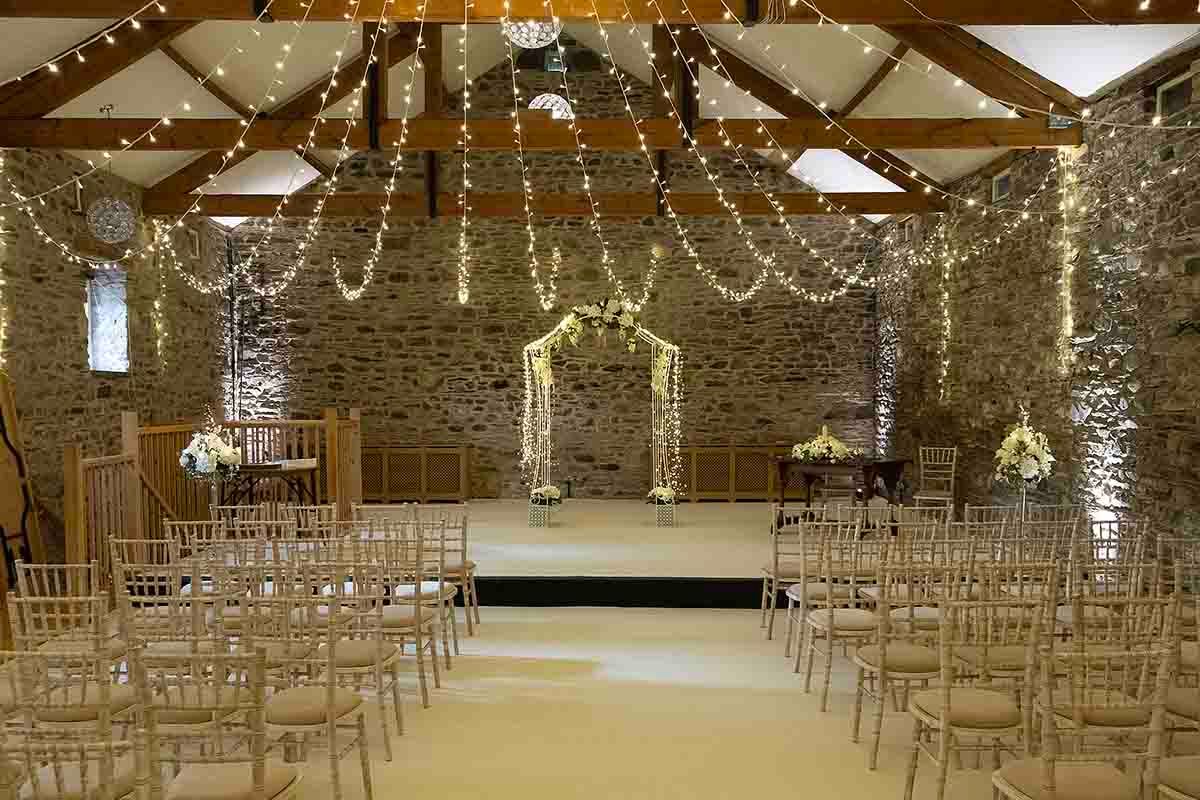 Elegant wedding ceremony venue at New House Farm near Cockermouth with fairy lights, floral arch, and gold chiavari chairs.