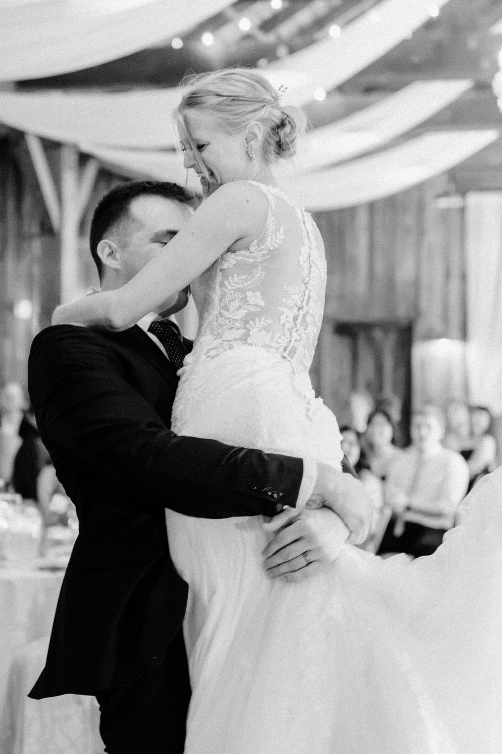 Groom lifting bride during first dance at wedding reception in black and white photo.