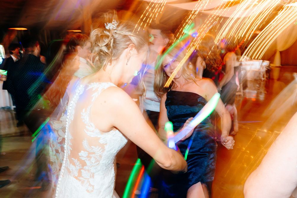 Bride dancing with guests holding glow sticks at a lively wedding reception with colorful light effects.