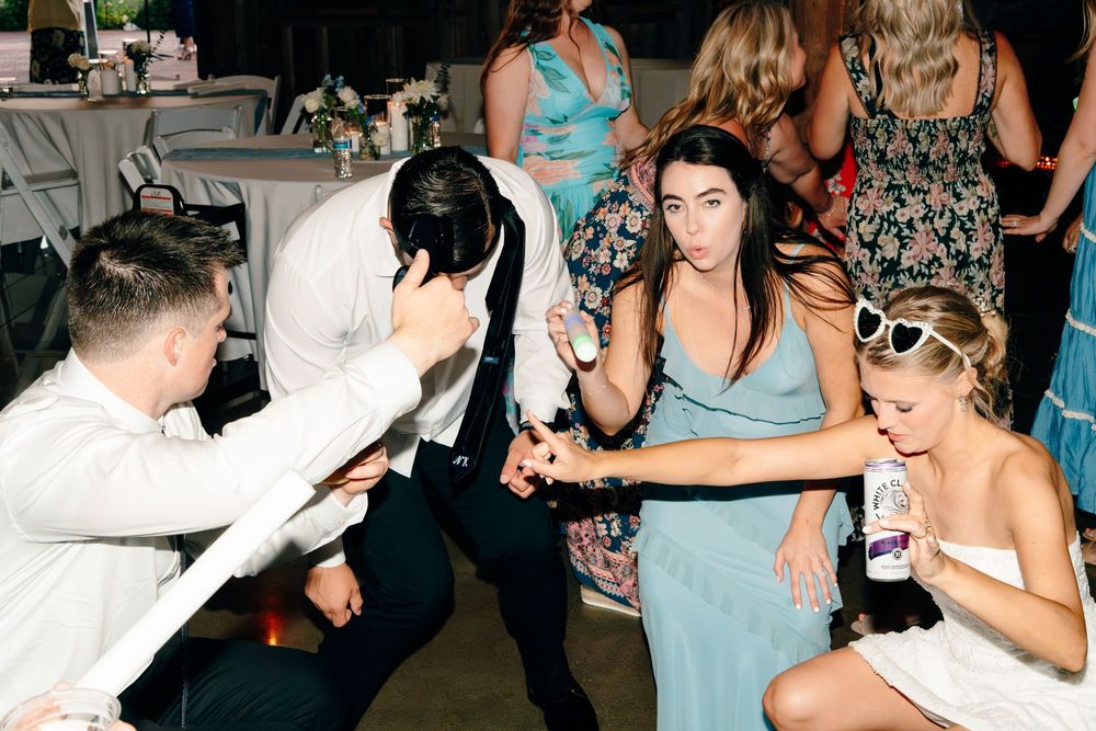 Wedding guests dance energetically at a lively reception party, with women in blue and white dresses.
