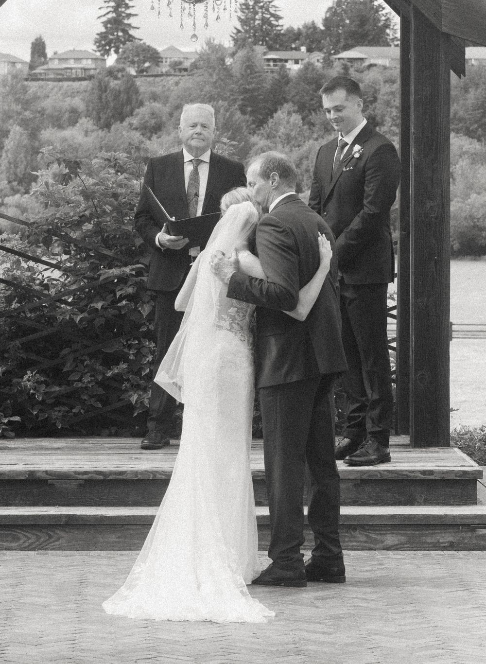 Black and white photo of a bride and groom sharing their first kiss at an outdoor wedding ceremony.