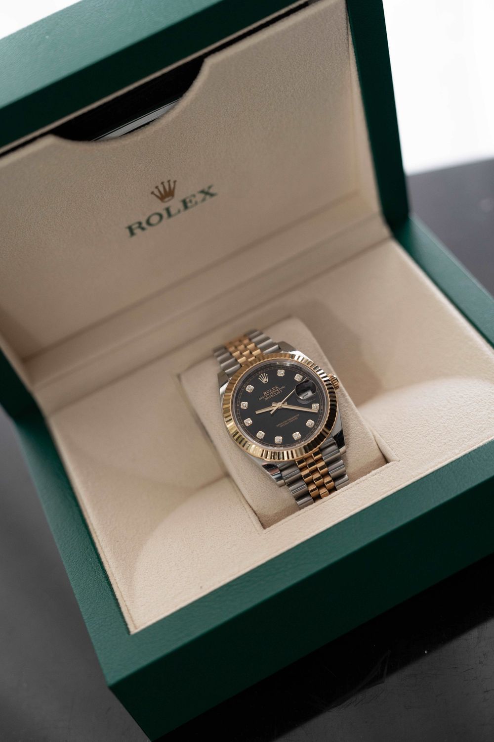 Rolex Datejust two-tone gold and silver watch with black diamond dial displayed in green luxury gift box.