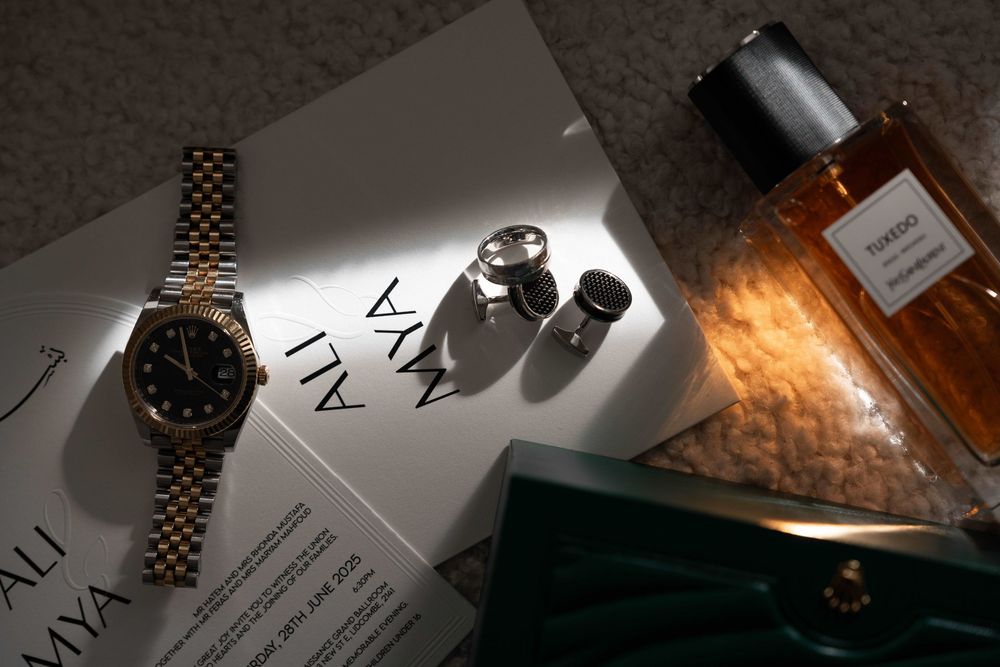 Luxury flat lay featuring a gold Rolex watch, cufflinks, amber cologne bottle, and green box on a magazine.