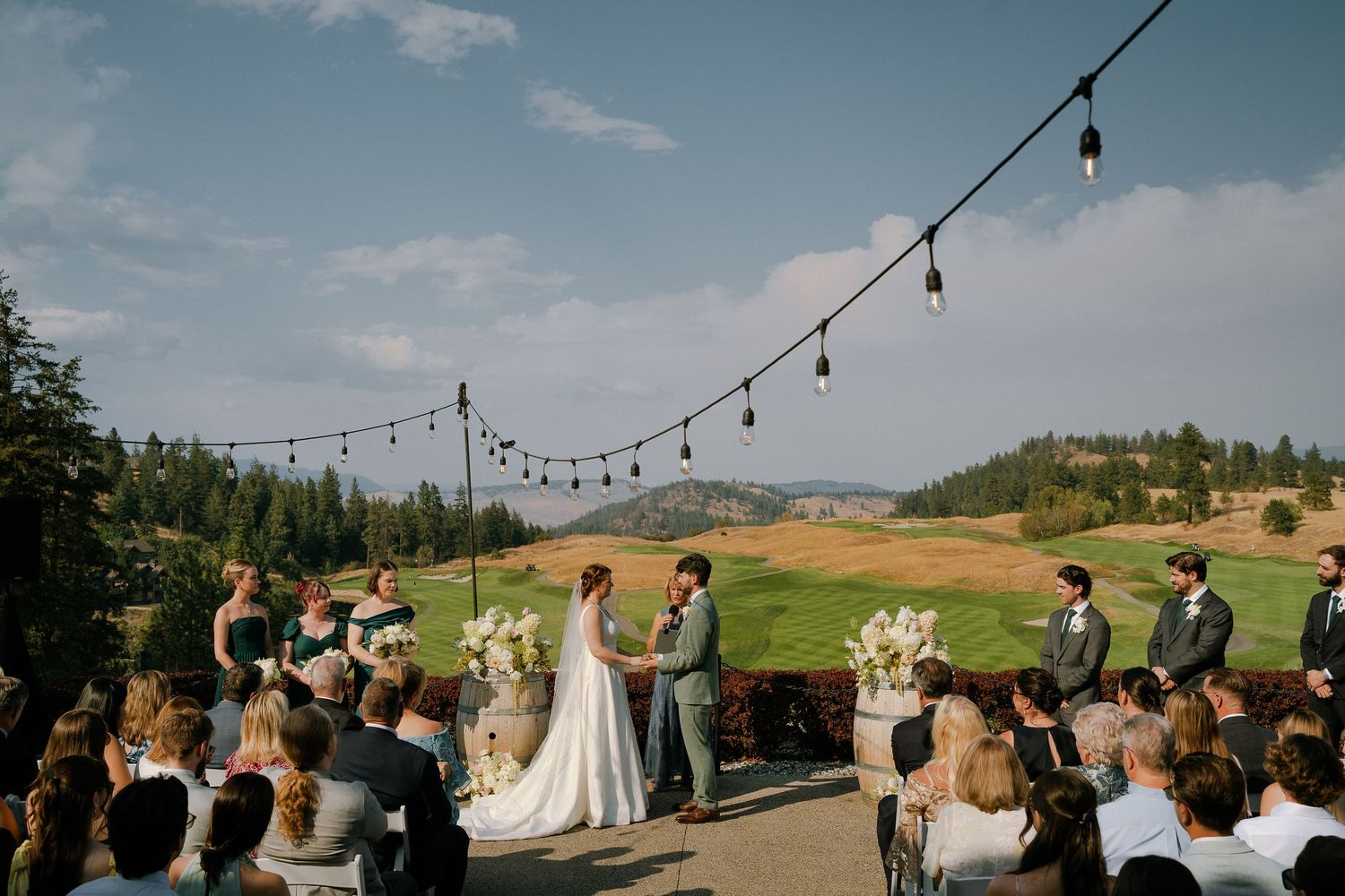 Outdoor wedding ceremony on predator ridge golf course with string lights, guests seated, couple at altar, surrounded by trees and hills.