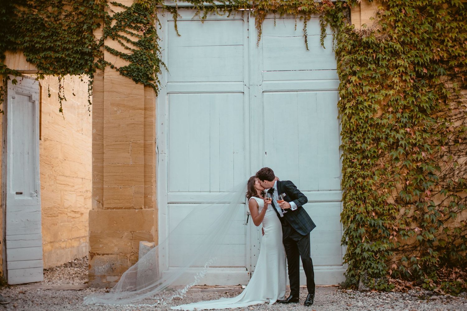 Beth and Matt kissing in front of tall pale doors framed by ivy.