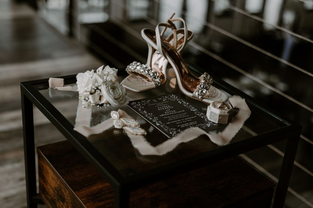 Wedding details flat lay with jeweled heels, garter, rings, and chalkboard sign.