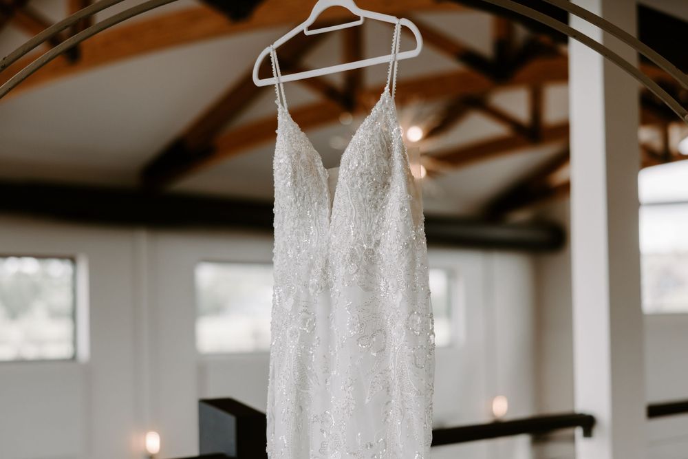 Elegant lace wedding dress with V-neckline hanging on hanger in rustic barn venue.