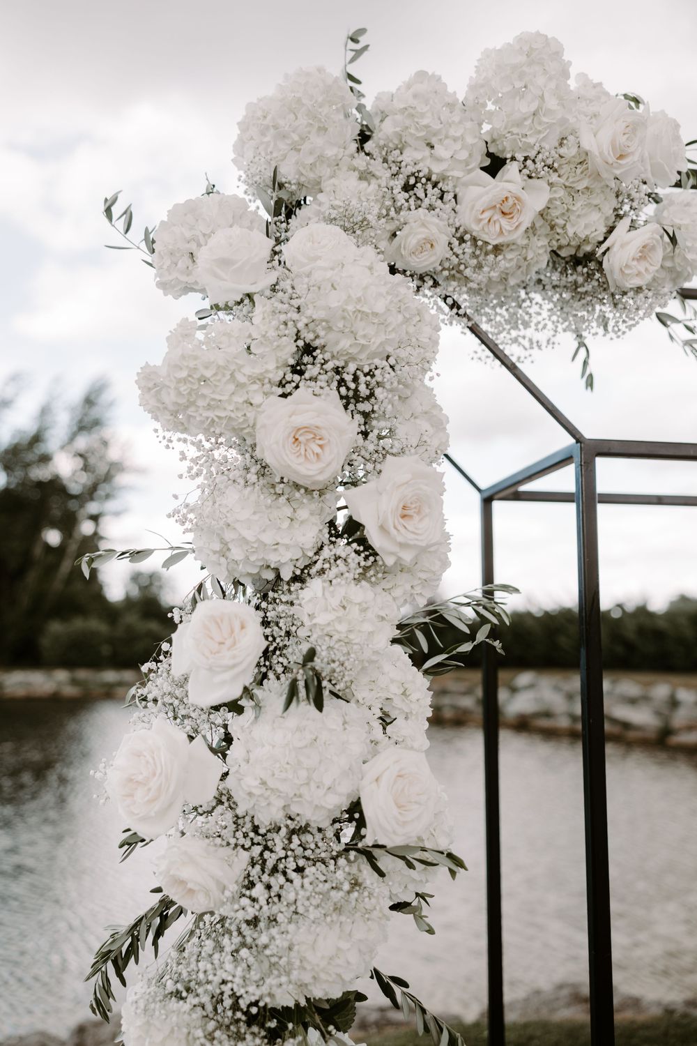 Elegant white rose and baby's breath floral arrangement on geometric wedding arch.