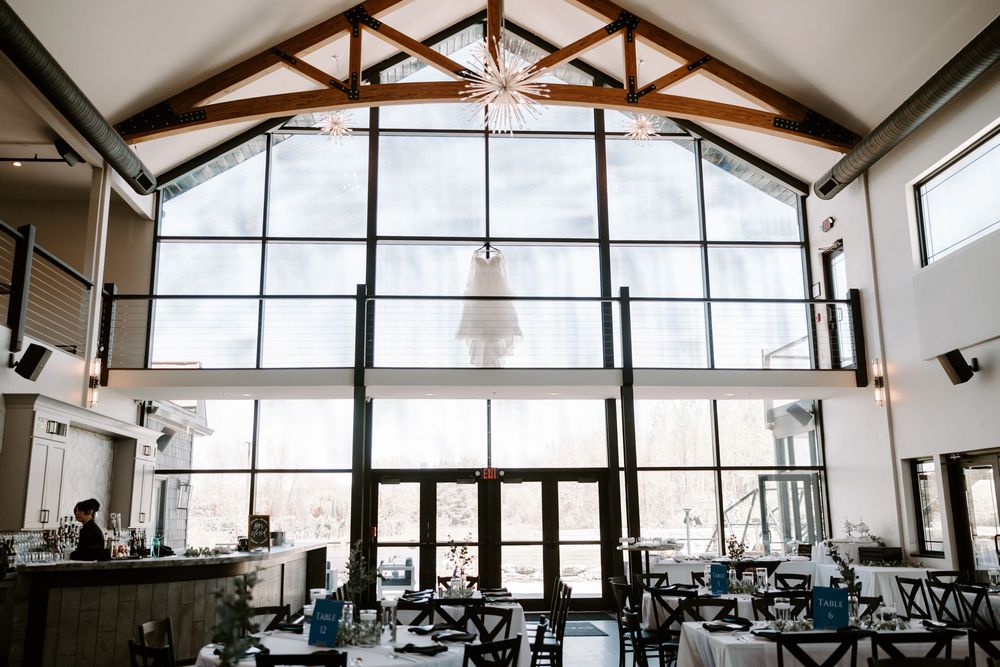 Elegant wedding venue with soaring vaulted ceilings, large windows, and a bridal gown hanging as a stunning centerpiece.