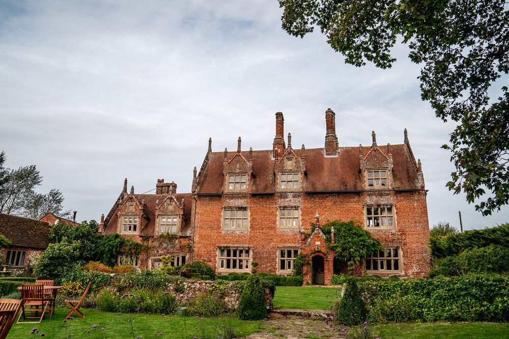 Historic red brick Tudor manor house with ornate chimneys surrounded by lush gardens.